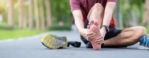 Runner sitting on pavement holding his foot in pain, showing signs of plantar fasciitis after exercise.